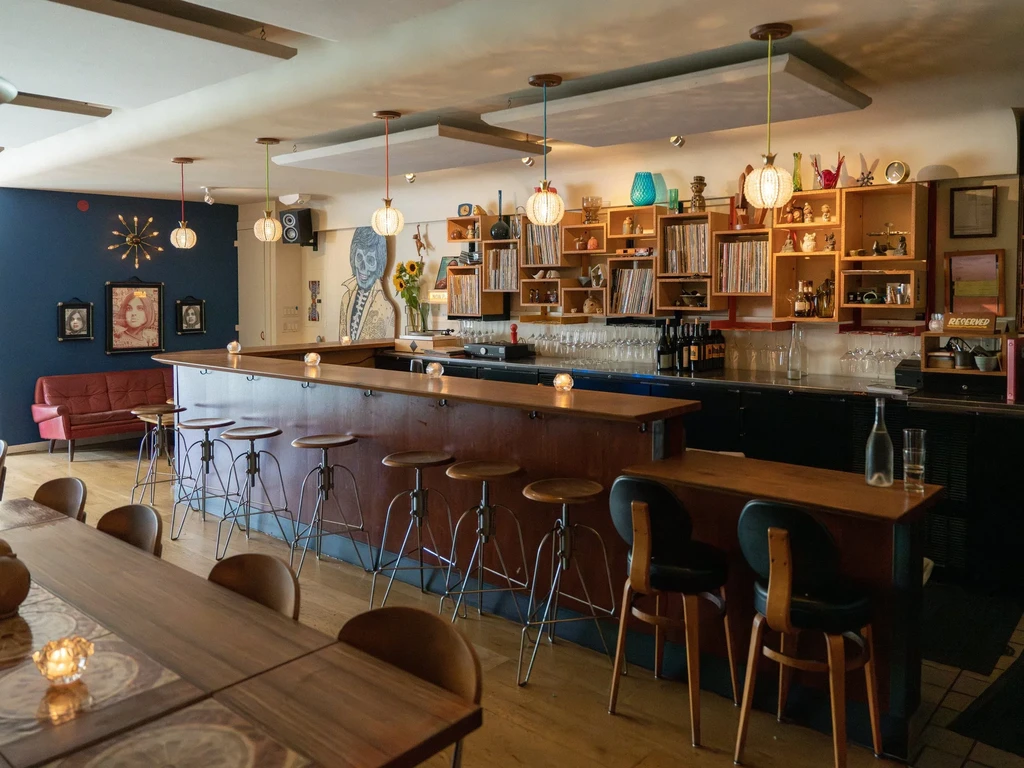 An eclectic bar interior with a long wooden counter and shelving.