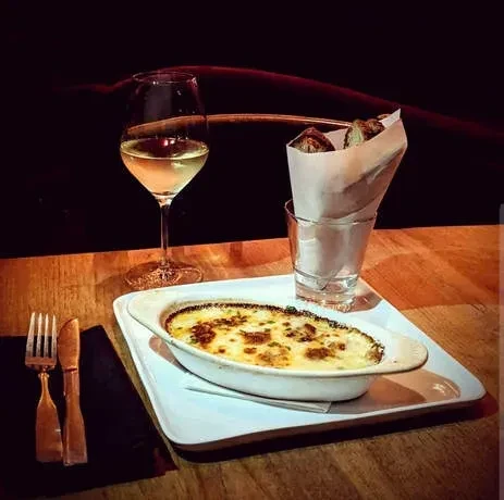 A dish of baked food, white wine, and bread on a wooden table.