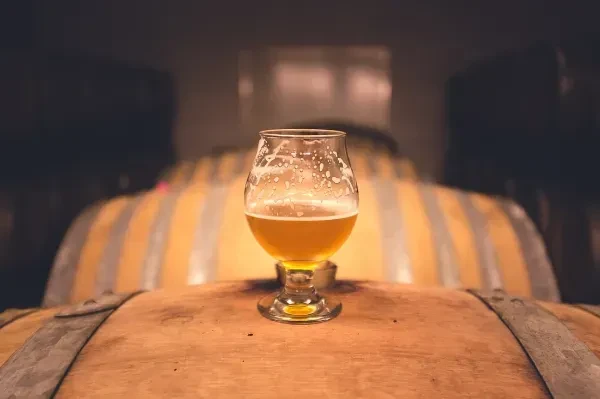 A partially consumed glass of beer sits atop a wooden barrel.