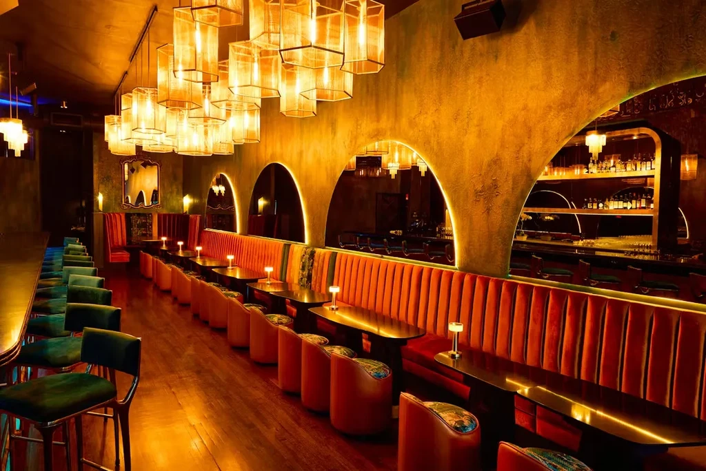 A luxurious, dimly lit bar with orange velvet seating and warm lighting.