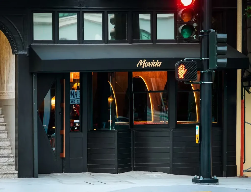 Black Movida restaurant with awning, red stoplight, and don't walk signal.