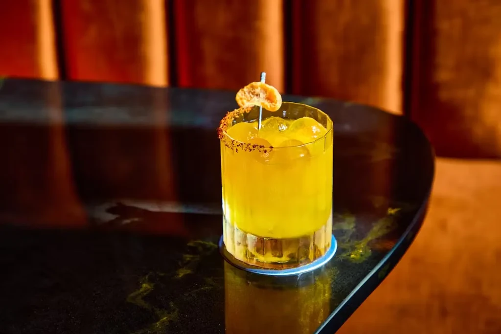A yellow drink in a glass with a spiced rim and fruit garnish.