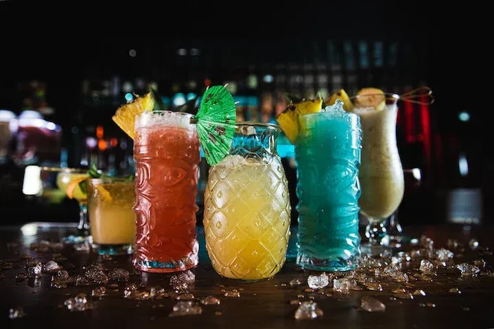 Colorful cocktails in decorative glasses on a bar, with scattered ice.