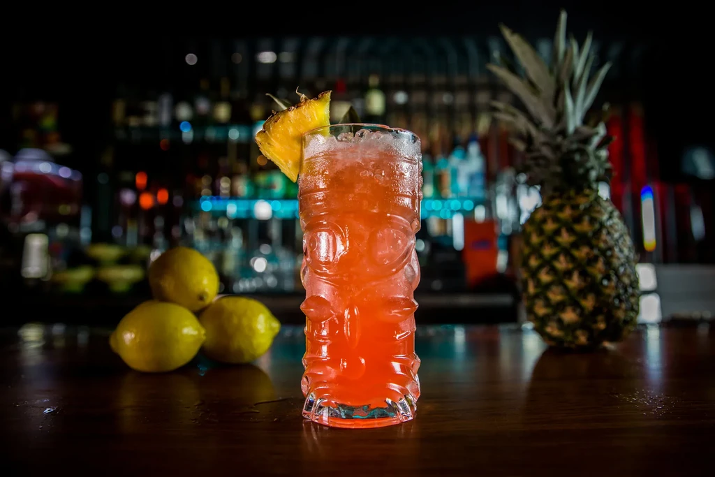 Iced tiki cocktail with pineapple garnish, lemons, and whole pineapple.