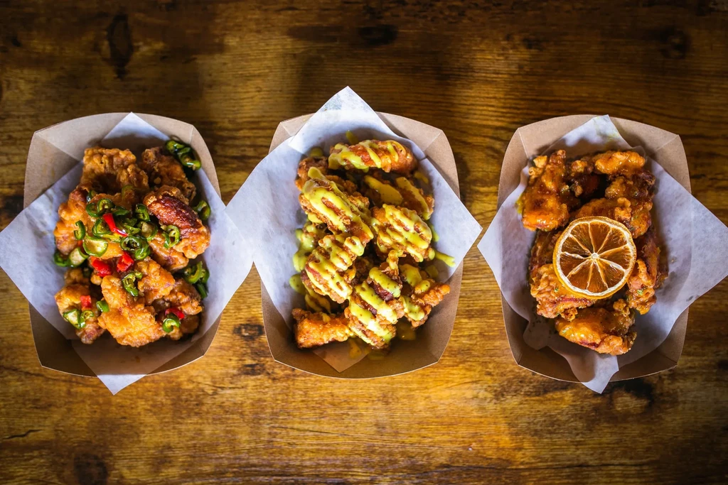 Three cardboard trays of popcorn chicken with various toppings.