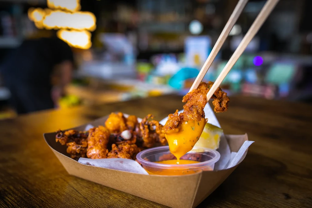 Chopsticks holding a piece of fried calamari dripping with sauce.