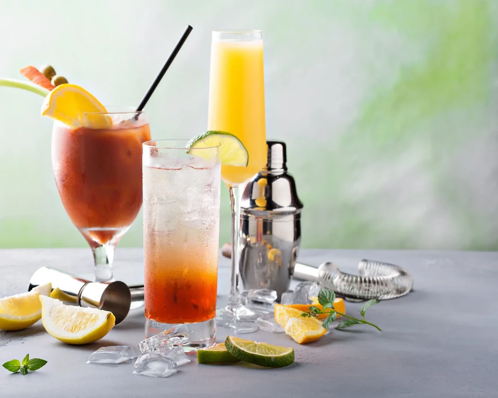 Three different cocktails with garnishes and bartending tools on a gray table.