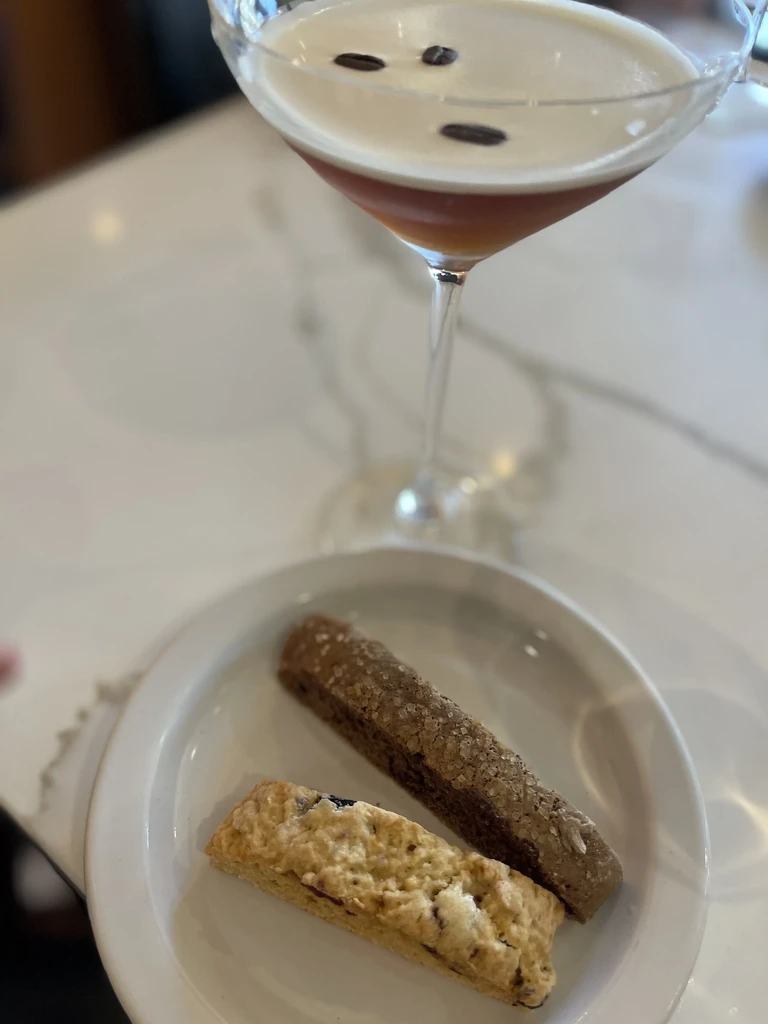 Espresso martini and two biscotti on a white plate and table.