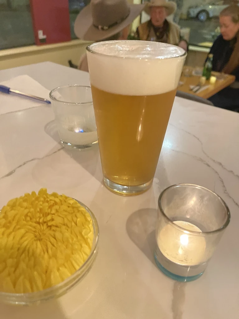 A beer, candles, and yellow flower on a white table.