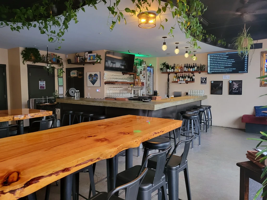 A bar area with seating, wooden tables, and hanging plants.
