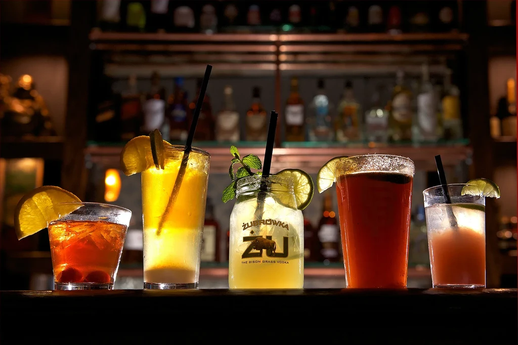 Five colorful cocktails and mixed drinks sit on a bar counter.