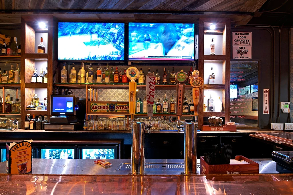 A well-stocked bar with two large TVs showing a basketball game.