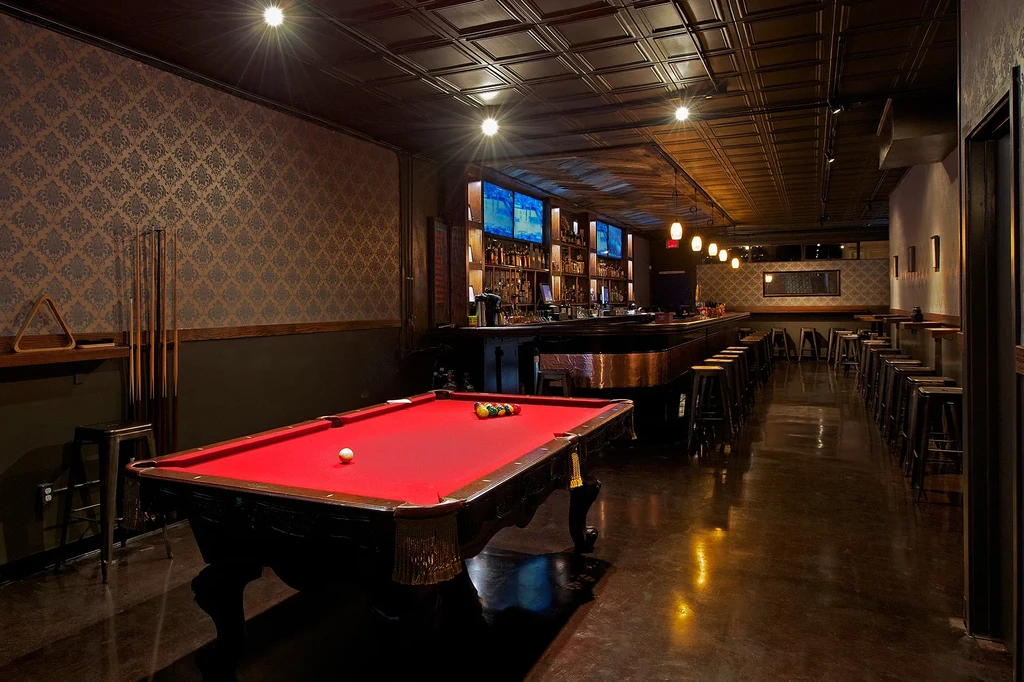 A dimly lit bar with a red pool table and long bar.