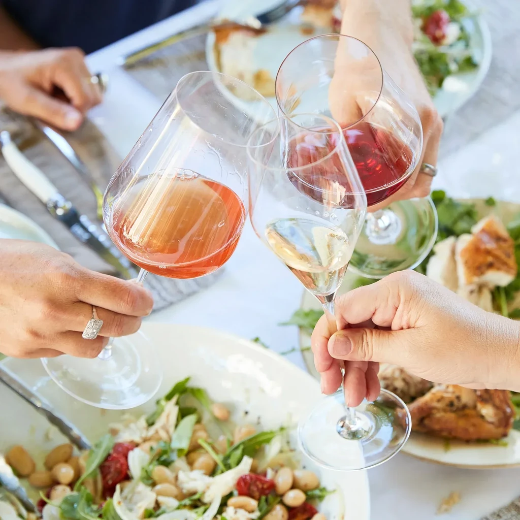 Four hands raise glasses of rosé, white, and red wine.