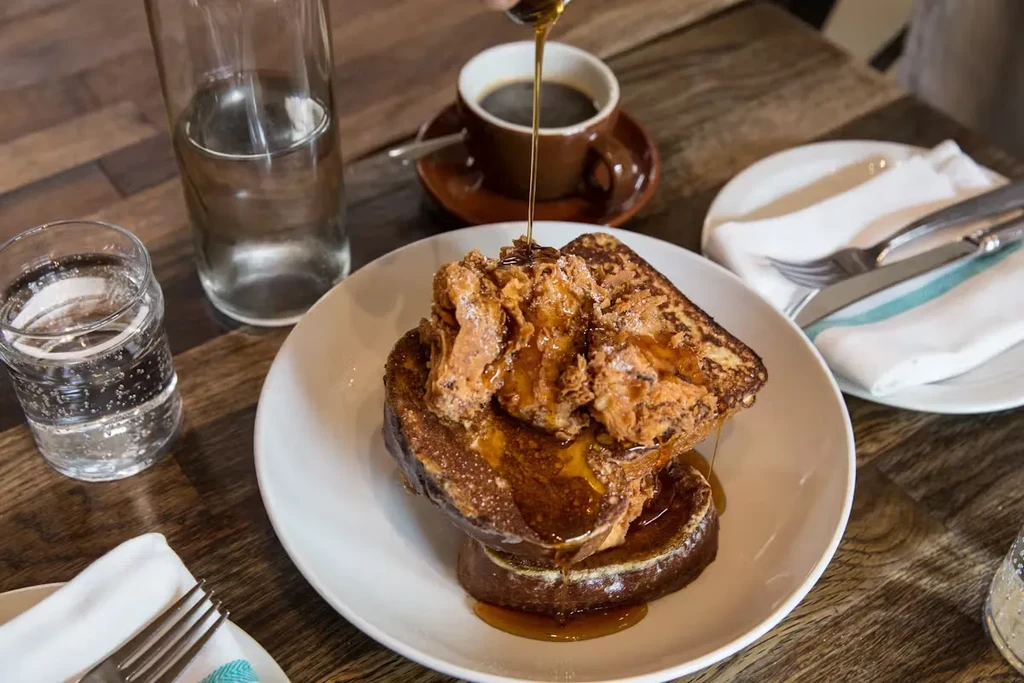 Syrup being poured over French toast with fried chicken on a plate.