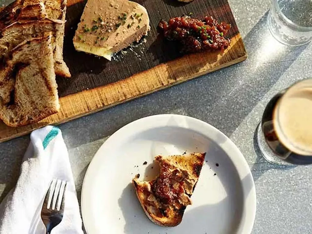 A charcuterie board with pâté, bread, and relish on a gray table.