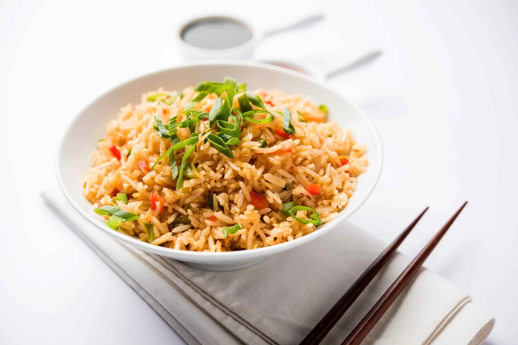 Fried rice in a white bowl with chopsticks and soy sauce.