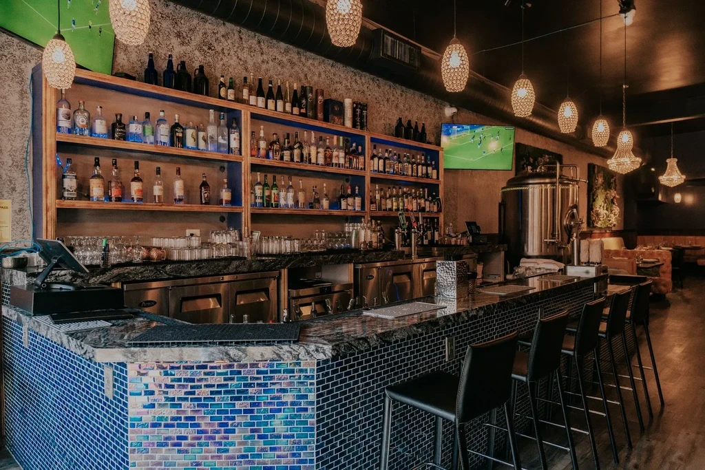 A vibrant bar with blue tile, liquor shelves, and hanging lamps.