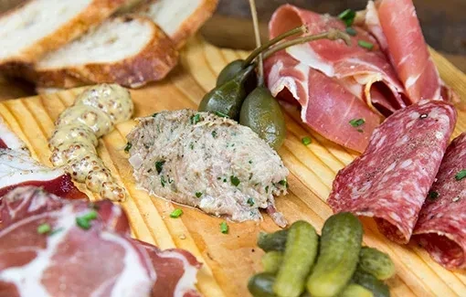A charcuterie board with various meats, pickles, mustard, and bread.