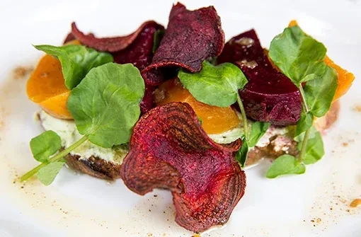 A dish of beets, beet chips, and greens on a white plate.