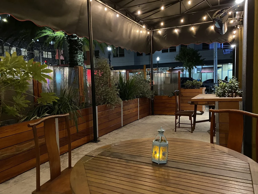 An outdoor restaurant patio at night with strung lights and potted plants.