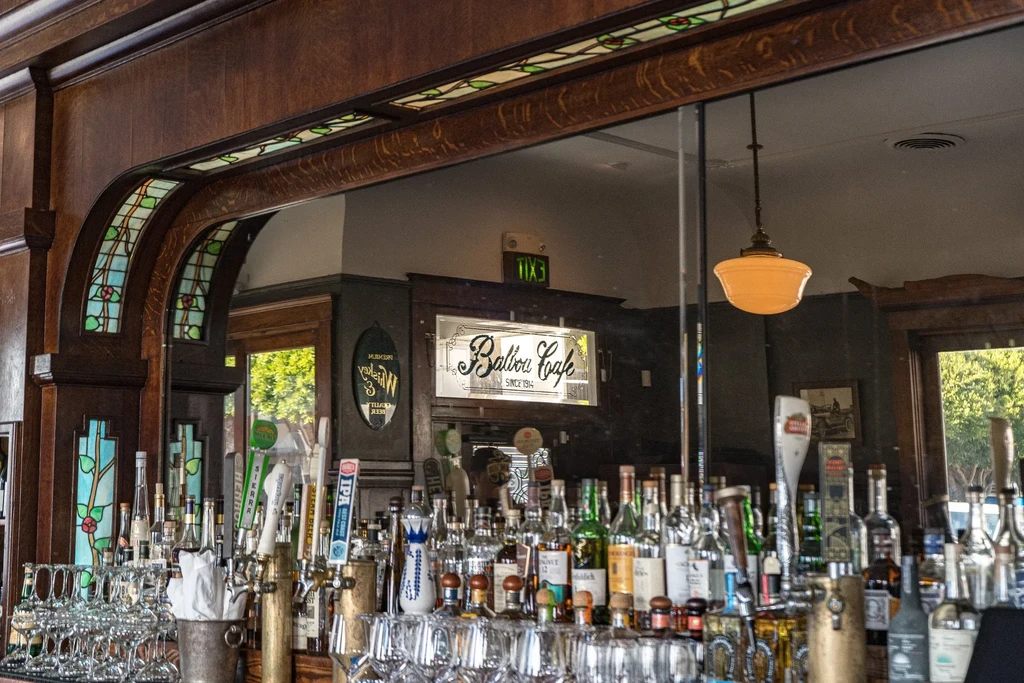 Bottles of liquor on a bar with stained glass and a "Balboa Cafe" sign.