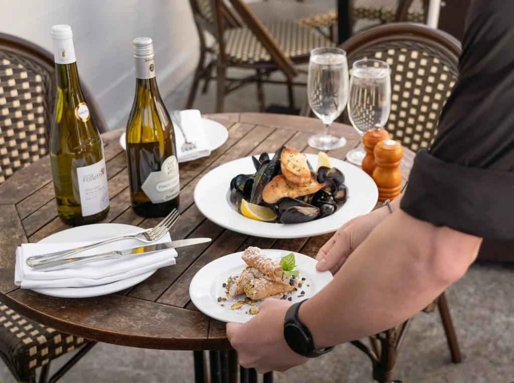 Hands setting down a plate of cannoli on an outdoor restaurant table.