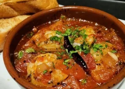 Shrimp in tomato sauce with herbs, chilies, and baguette slices.