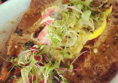 Close-up of a cooked pork chop with herbs and lemon slices.