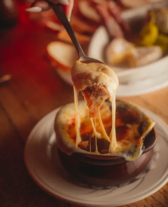 Hand lifting spoon of cheesy soup from crock on plate.