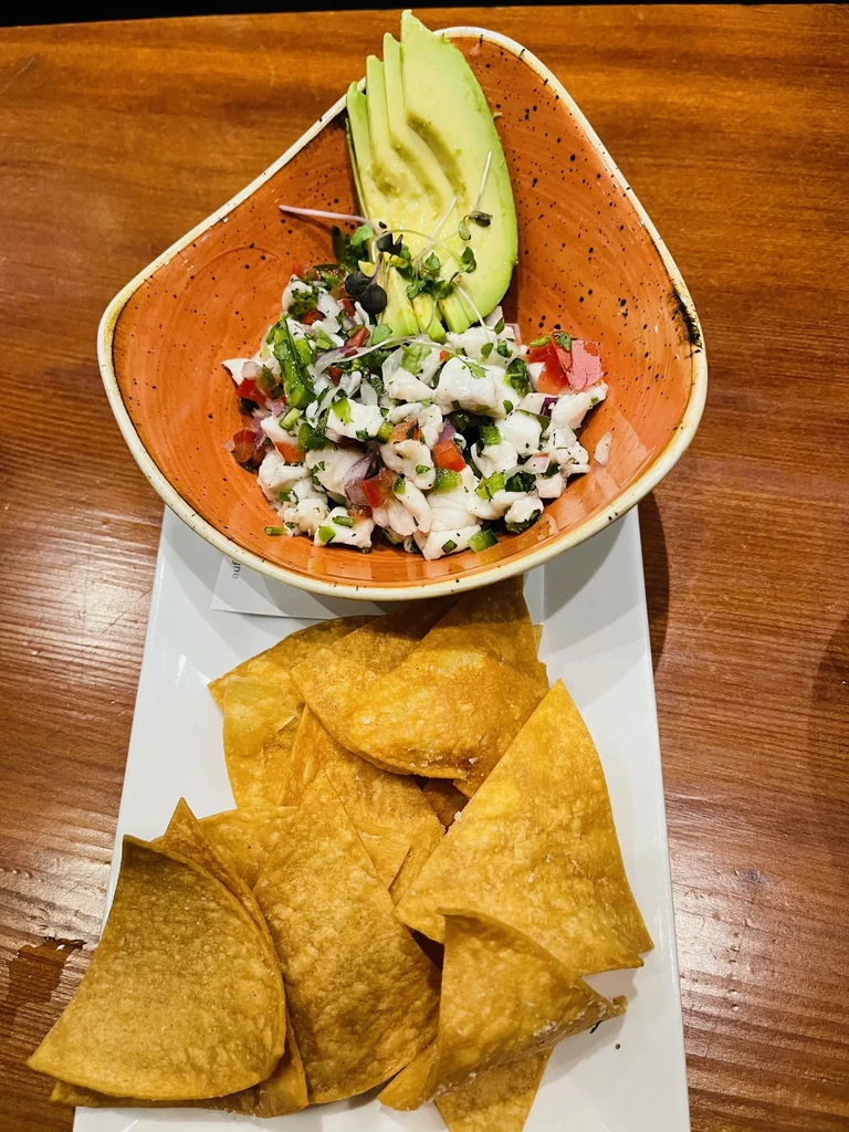 Ceviche with avocado, microgreens, and tortilla chips on a wooden table.
