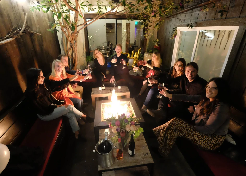 People smile around a bright fire pit on a nighttime patio.