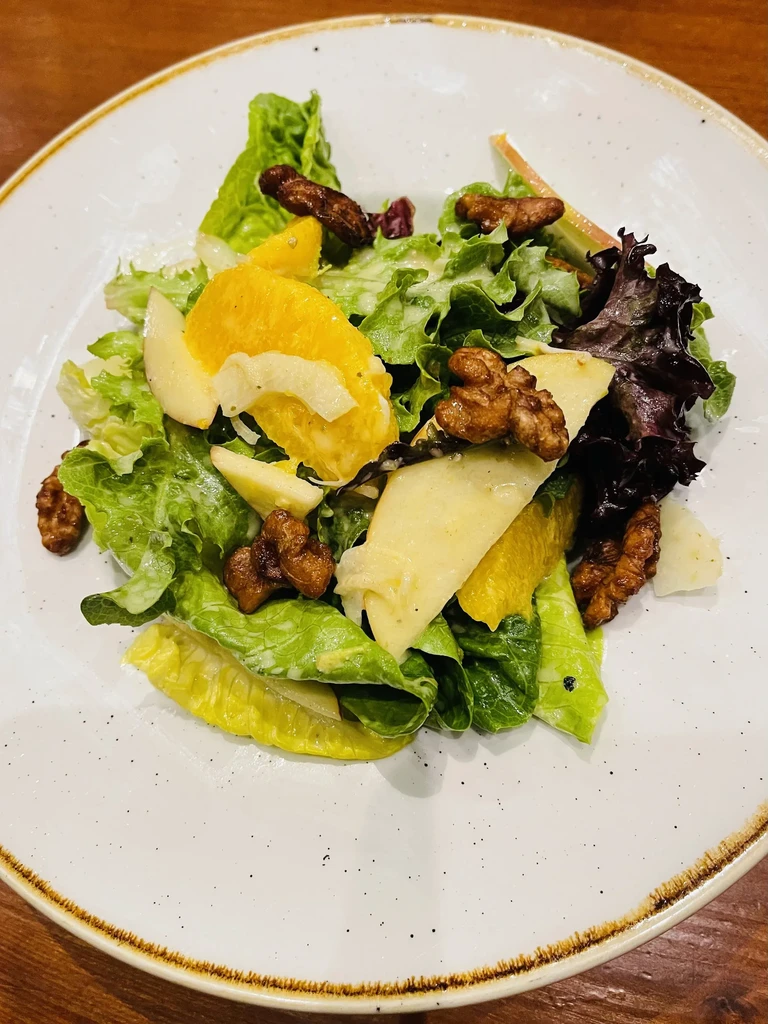 Fresh green salad with orange, apple, walnuts on a white plate.