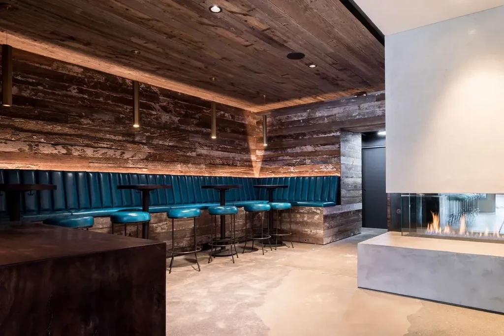 A modern bar with a wooden interior, teal booths, and a fireplace.