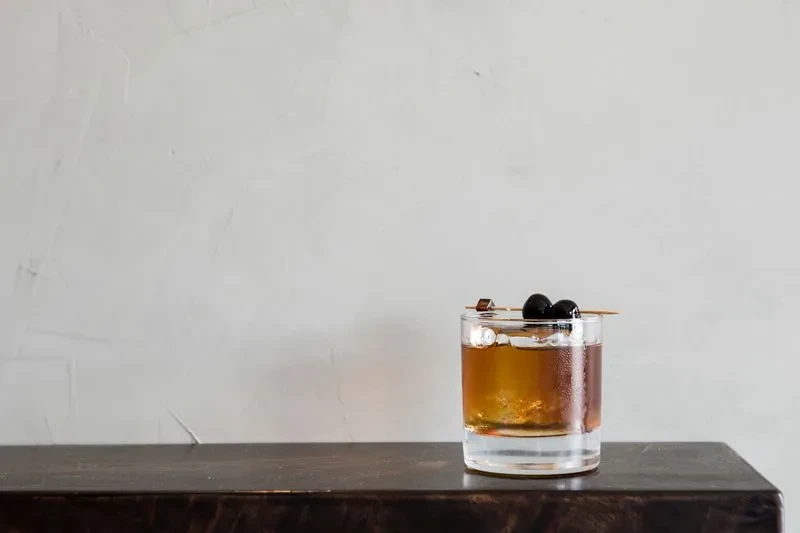 A cocktail with cherries and a sugar cube on a wooden surface.