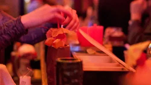 Person decorating a cocktail with an umbrella at a bar.