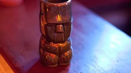 A dark brown tiki mug on a reddish-brown surface.