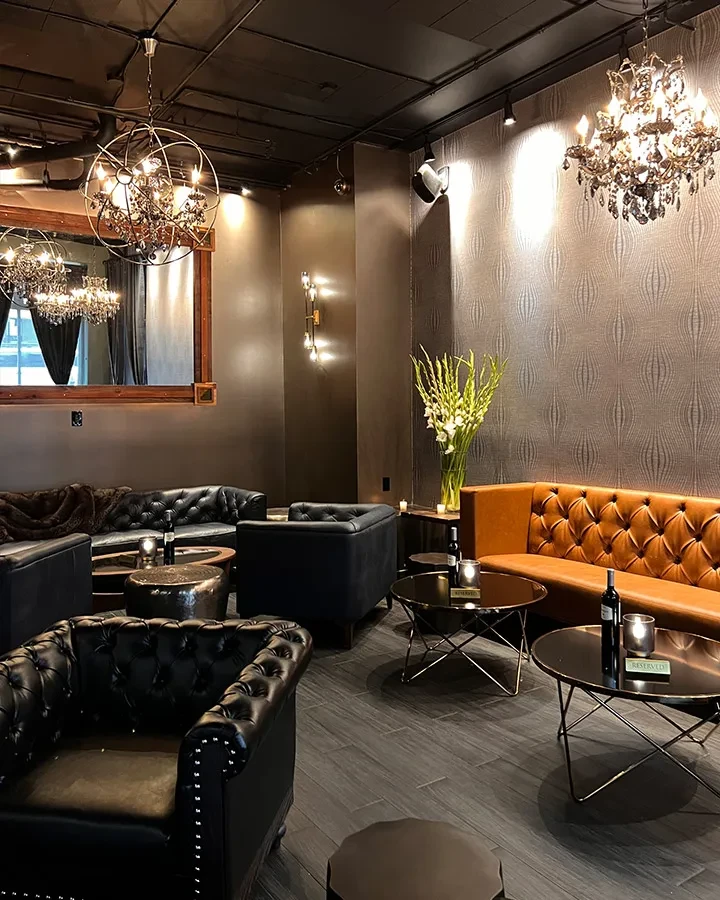 A dimly lit upscale lounge with leather seating and chandeliers.