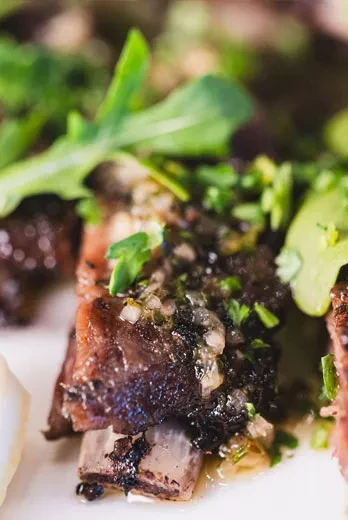 Close-up of braised short ribs with sauce and green garnish.