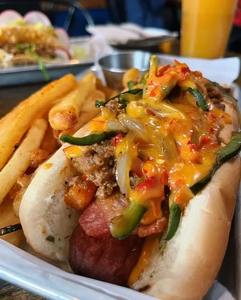 A hot dog in a bun, topped with cheese, peppers, and ground beef.