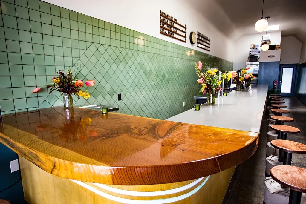 A long, empty bar with a shiny wooden counter and green tiled wall.