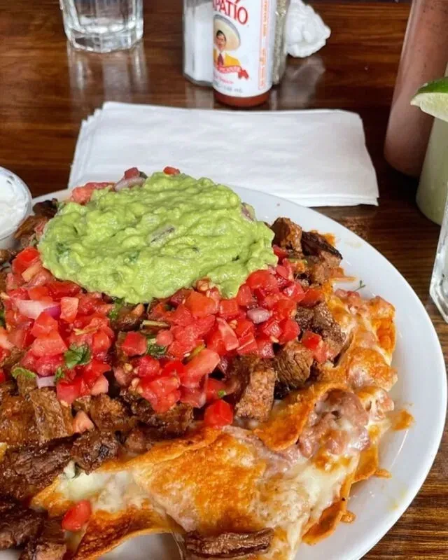 A close-up of a plate of loaded nachos with guacamole and pico de gallo.
