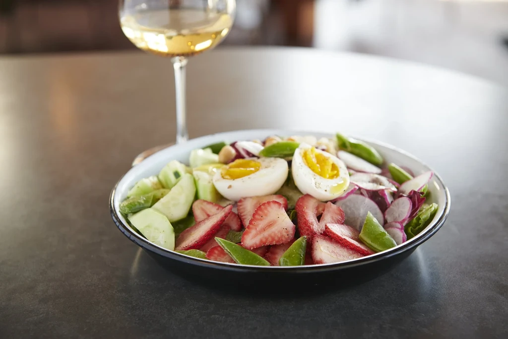 A bowl of salad with eggs, strawberries, cucumbers, radishes and wine.