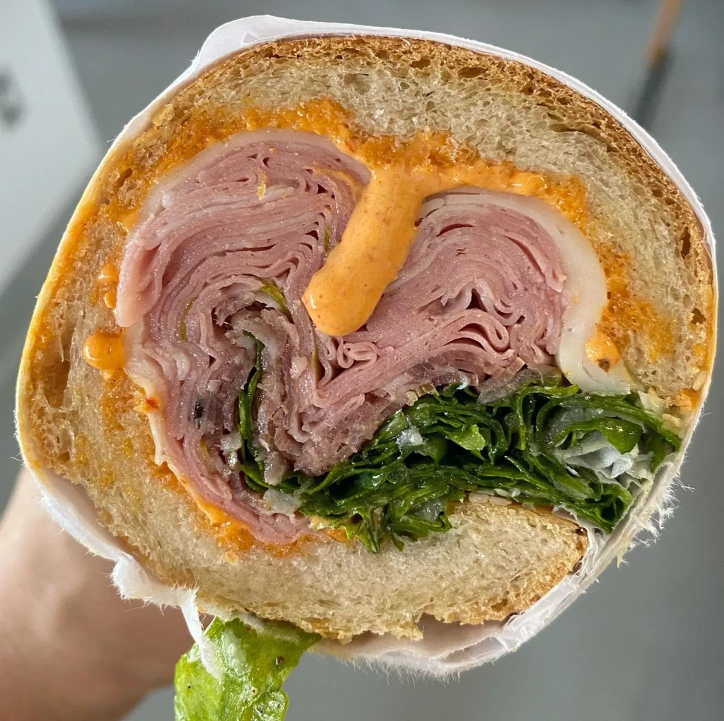 Close-up of a halved sandwich with meat, cheese, lettuce, and sauce.