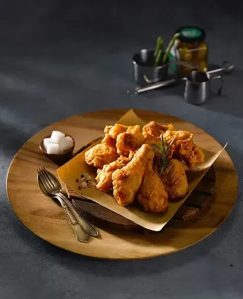 Golden fried chicken pieces with rosemary on a wooden plate.