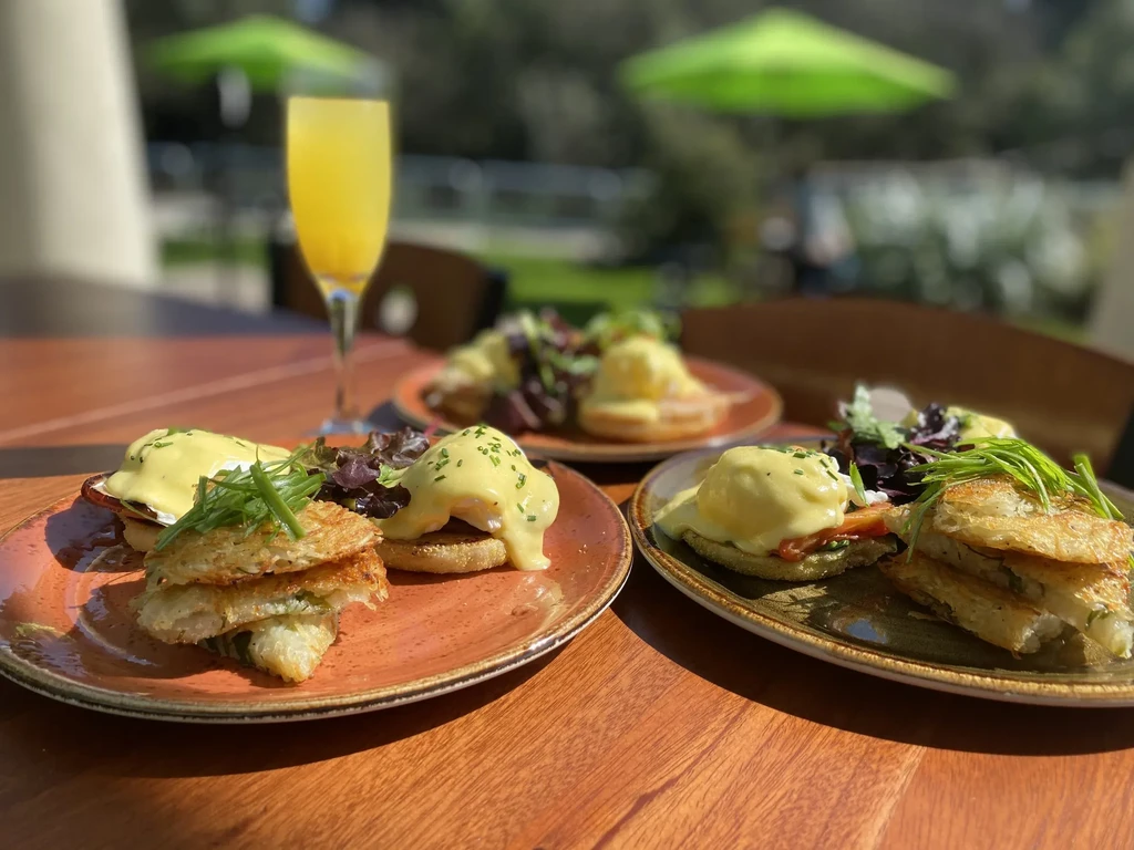 Multiple plates of eggs benedict and drinks at an outdoor brunch setting.