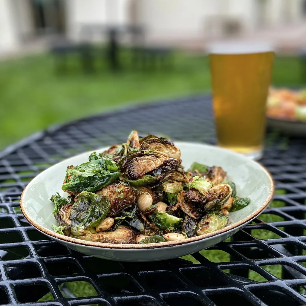 A bowl of roasted Brussels sprouts with almonds and a beer.