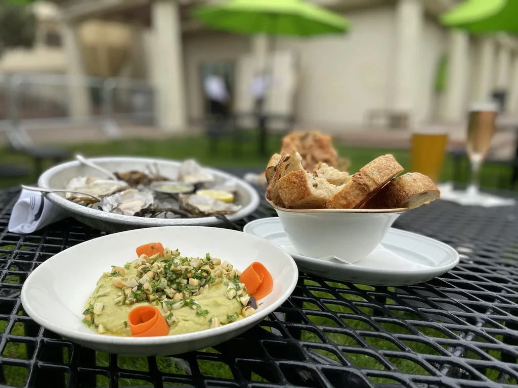 Outdoor dining with oysters, hummus, and bread on a black metal table.