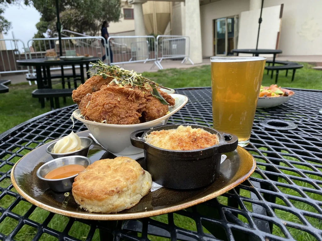 Fried chicken, mac and cheese, biscuit, and beer on outdoor table.
