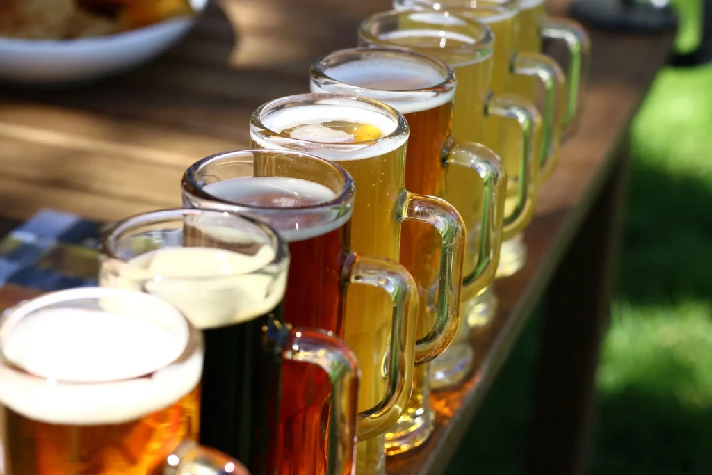 A line of beer mugs filled with different colored beers on a wooden table.